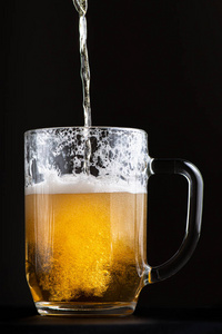 新鲜明亮的啤酒被倒入一个大的玻璃高脚杯中。在黑色背景上隔离浅景深的选择性聚焦宏镜头