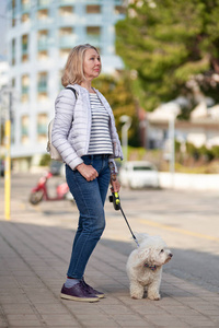夏日城，一位金发碧眼的中年妇女牵着毛茸茸的白狗散步