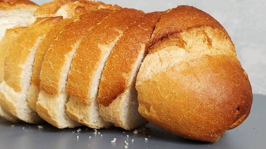 小麦粉切片的面包。香喷喷的白面包片和酥脆的烤面包皮。含有面筋的产品。新鲜面包。灰色背景。面包屑在桌子上。