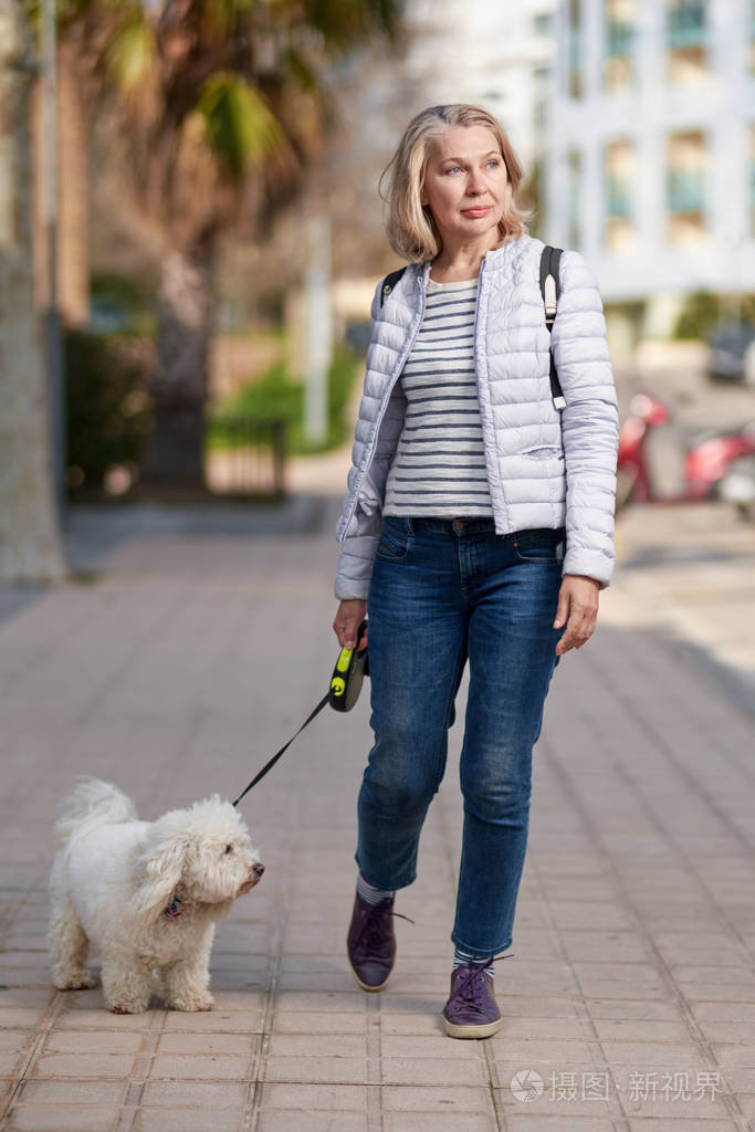 夏日城一位金发碧眼的中年妇女牵着毛茸茸的白狗散步