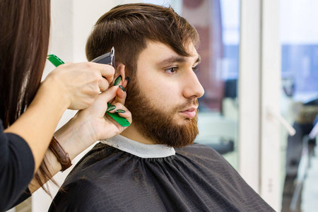理发师为男性客户理发，留胡子的男子使用专业理发工具，理发师工作空间工作场所的设备。理发师服务。理发店理发，修胡子。
