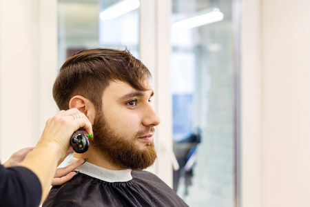 理发师为男性客户理发，留胡子的男子使用专业理发工具，理发师工作空间工作场所的设备。理发师服务。理发店理发，修胡子。