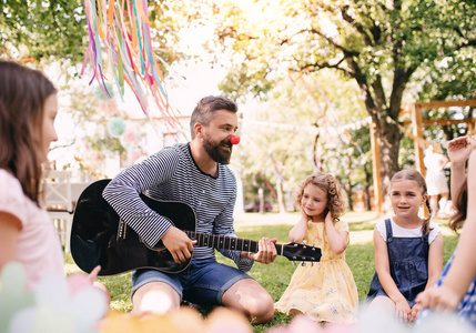 夏天，一个男人带着小孩在室外的花园里弹吉他。