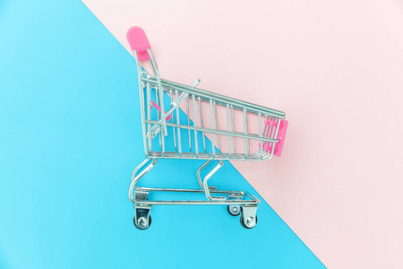 小型超市购物推车购物玩具与车轮隔离在蓝色和粉红色粉彩彩色时尚几何背景复制空间。商城商城商城商铺消费理念。