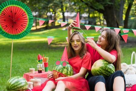 两个漂亮的少女在公园里吃西瓜玩得很开心。天气晴朗。夏季概念。西瓜派对，野餐，白天