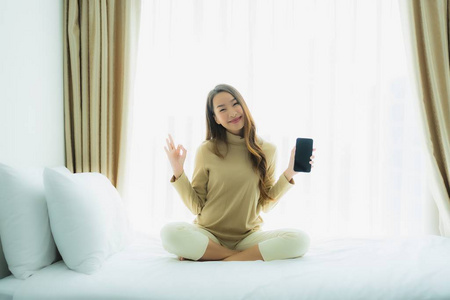 年轻的亚洲女人在床上用智能手机
