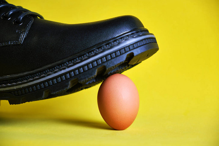 黄底黑靴子踩在一个易碎的鸡蛋上.观念,无力的防卫,关心和监护.照片