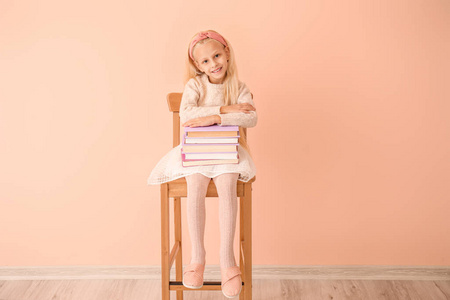 拿着书的小女孩坐在彩色墙上的椅子上