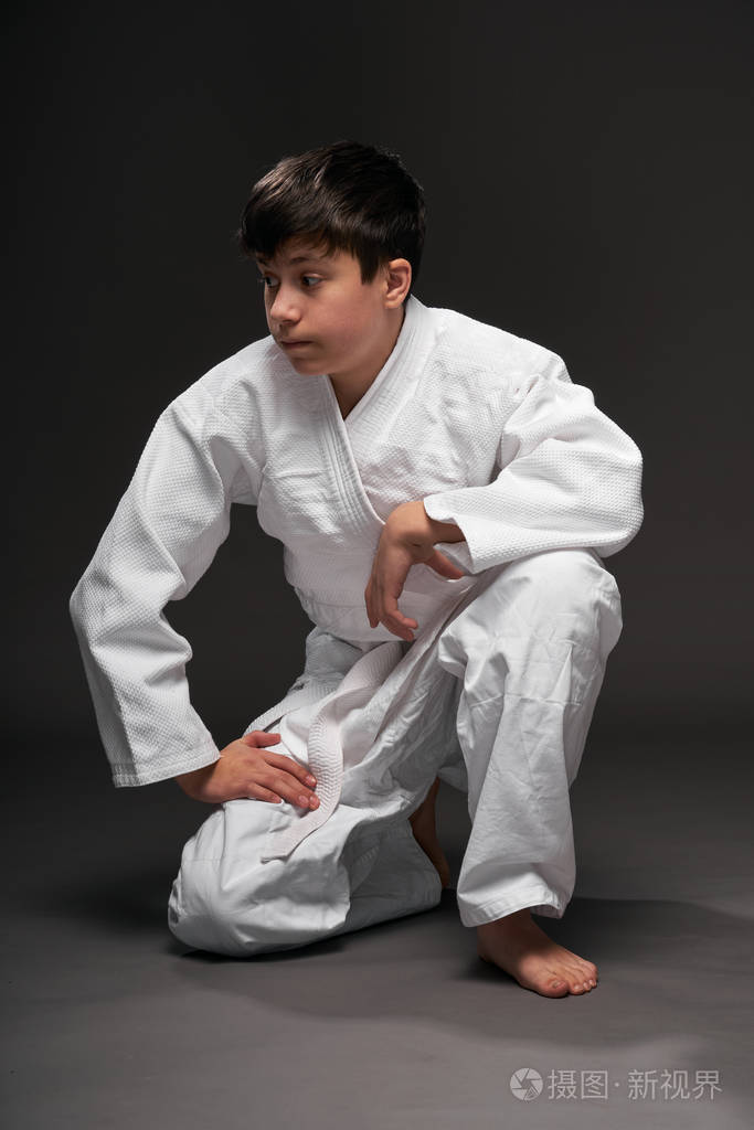 一个穿着武术服的少年坐在深灰色的背景上思考这是一个体育概念