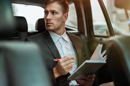 年轻的成功商人坐在车里与合作伙伴见面时，会给他的计划者做笔记，这是一个多任务的概念