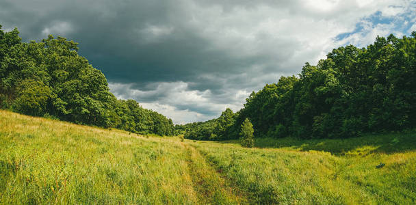 风景如画，蜿蜒曲折的山峦，有田野道路和暴风雨前的天空。大全景