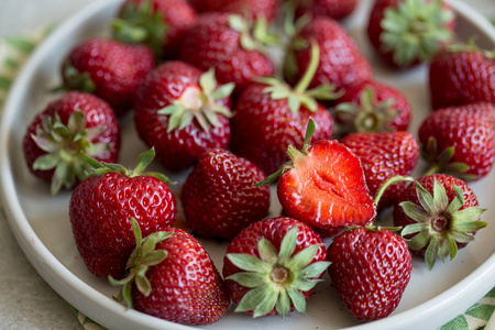 成熟多汁的草莓放在一个粘土盘子里，在浅色的背景上