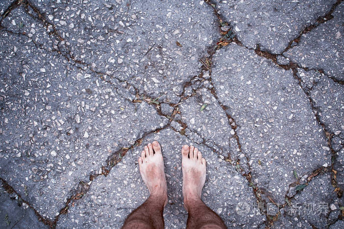 男人赤脚踩在破裂的沥青地板上