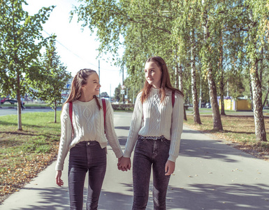 两名女生女朋友1214岁，在暑期公园散步，背道大树，牵手，欢笑，谈笑风生，放学归来，回家路上。积极放松的情绪。