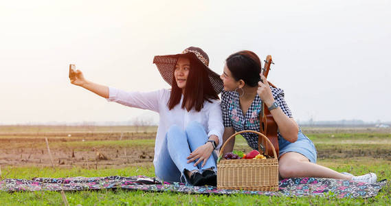 一群亚洲朋友在夏天玩Ukelle，花时间野餐假期。他们是快乐和自拍，放松时间的度假概念旅游