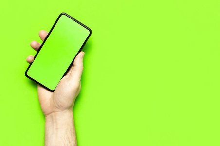 男性手持一部现代黑色智能手机，屏幕为绿色霓虹灯绿色背景平放俯视图。现代科技，手机，小玩意，触摸屏，设计模板。模型