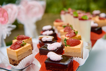 糖果棒上有草莓和巧克力蛋糕，奶油甜点放在玻璃杯里，放在户外的桌子上。生日宴会的甜点。假日概念