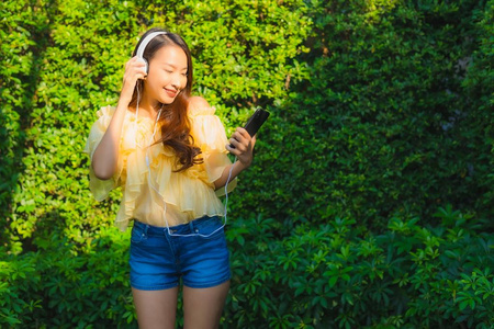 年轻的亚洲女人用智能手机和耳机给李