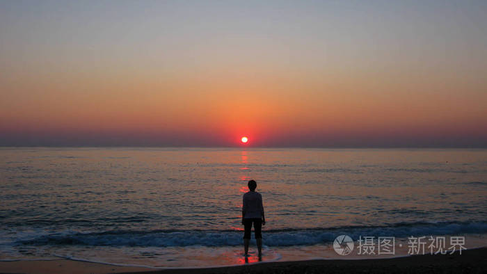 晴朗的蓝天大海太阳和黎明时分海边一个人的轮廓