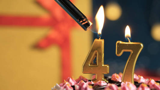 47号生日蛋糕用打火机点燃金色蜡烛,背景礼物黄色盒子系上红丝带.