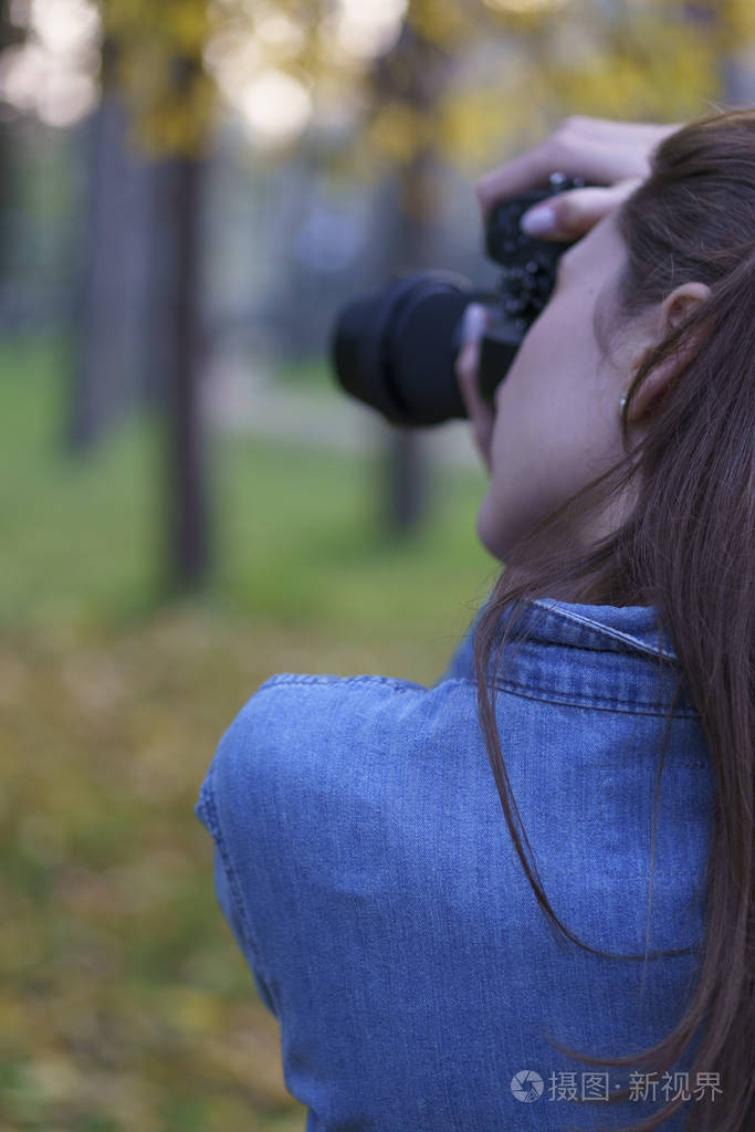 一个女人在一个美丽的秋天公园的背景下用一个黑色的小型照相机拍照