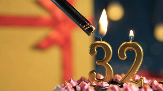 打火机点烟特写生日蛋糕32号由打火机点燃的金色蜡烛,背景礼物黄色