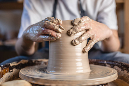 陶工在陶工的轮子上做花瓶。在一个车间里，一个女人用手在制作罐子。闭合