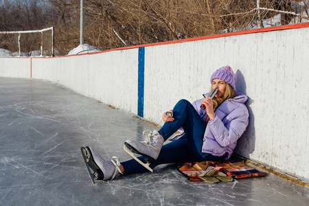 可爱的年轻女子在溜冰场上滑完冰，喝着热腾腾的热饮后放松。