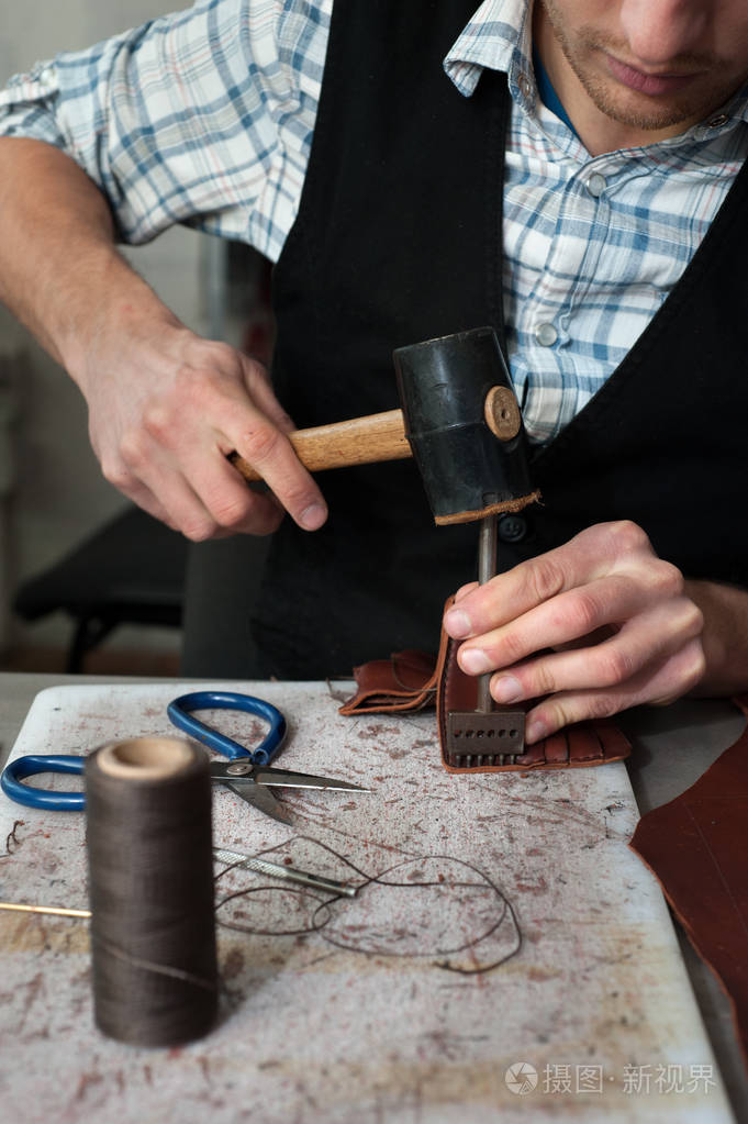 皮革工匠用锤子和天然皮革一起工作的特写镜头手袋师傅在当地车间工作
