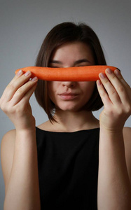 一个年轻的女孩手里拿着一个漂亮的胡萝卜。垂直照片