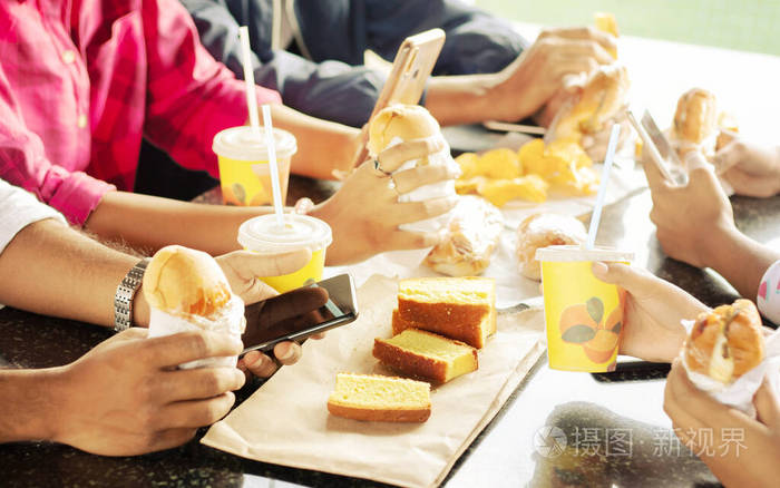 一群人坐在大学餐厅里吃着零食忙着用手机朋友们在一起吃饭开心聚会或