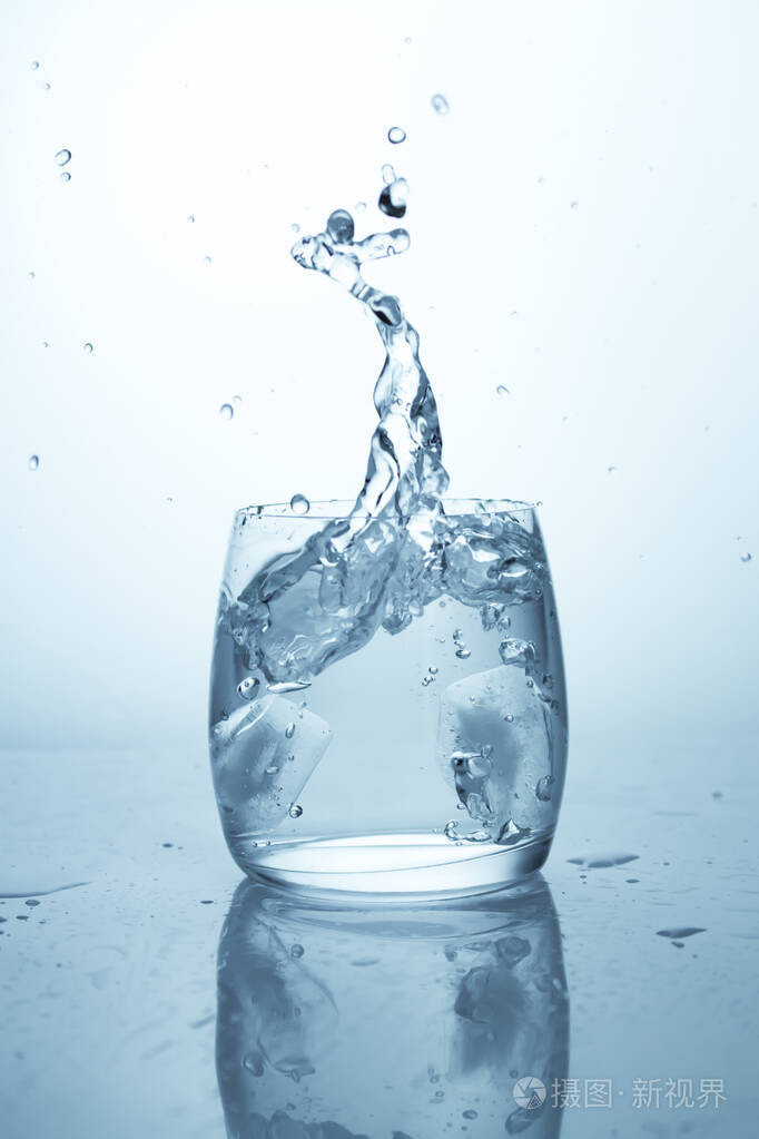 漂亮的水花冰块掉进水里一个盛着干净饮用水的玻璃杯还有一个水花飞溅