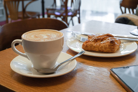 在一张木制的桌子上的盘子里放着卡布奇诺和饼干的杯子。在咖啡馆吃早餐。休息时间。