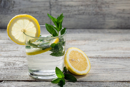 在木制背景的玻璃杯中加入柠檬和薄荷的水。夏季新鲜柠檬水饮料