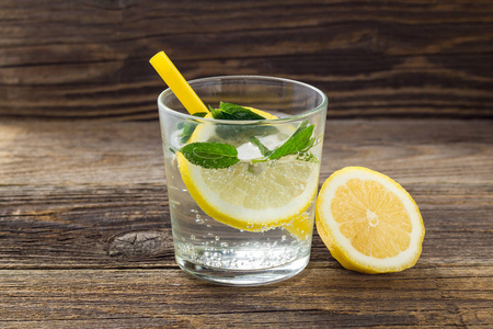 在木制背景的玻璃杯中加入柠檬和薄荷的水。夏季新鲜柠檬水饮料