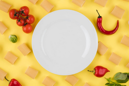 Empty plate on yellow background with pasta, tomatoes, pepper.