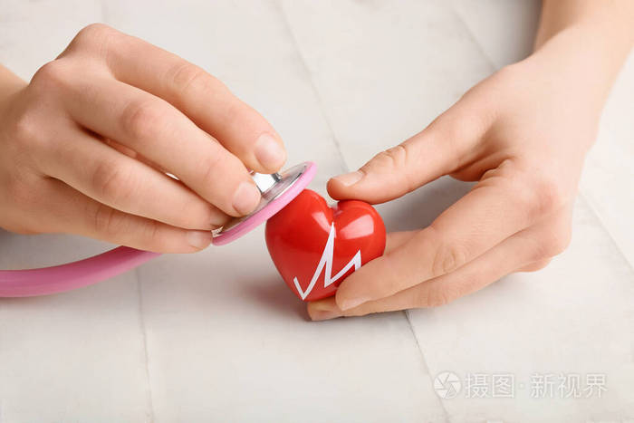 白色木质背景上红色心脏和听诊器的女性手心脏病学概念