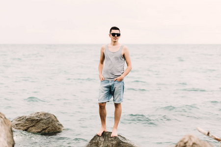 一个穿着t恤和短裤的年轻人站在沙滩上的大石头上