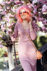 美丽的年轻女子，粉红色卷发，戴着墨镜，在盛开的春树旁。