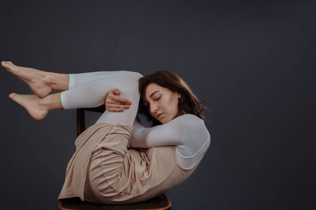 一个穿着简单衣服的女孩蜷缩在椅子上.在灰色背景的摄影棚里拍摄.照片