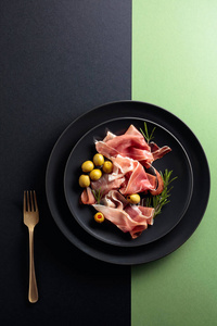 Prosciutto with rosemary and green olives on a black plate. Top 