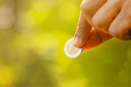 Hand holding Thai coin 10 Baht on green nature blur background. 