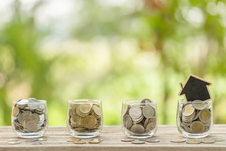 Wooden house model and coin in clear jar on wooden table. Money 