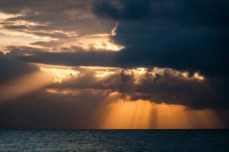 橘黄色的阳光穿过海面上乌云密布的天空照片