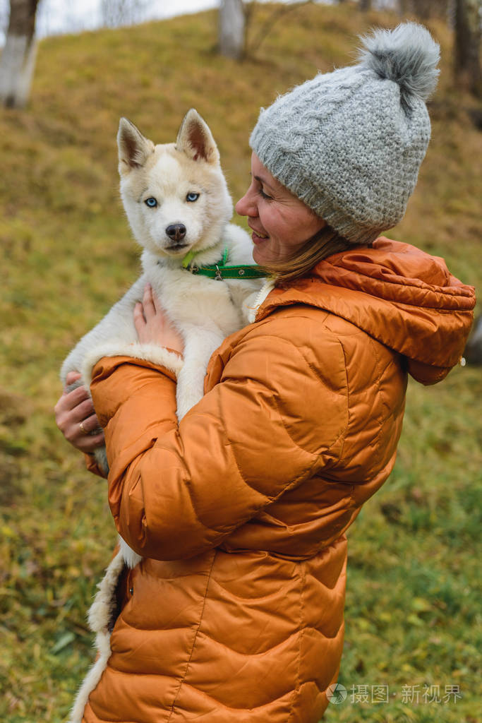 一个女人喜欢并抱着一只棕色和灰色的哈士奇小狗