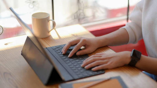 Cropped shot of college girl typing on digital tablet while work