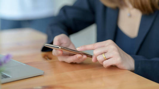 Close up view of a woman touching on smartphone on wooden desk 