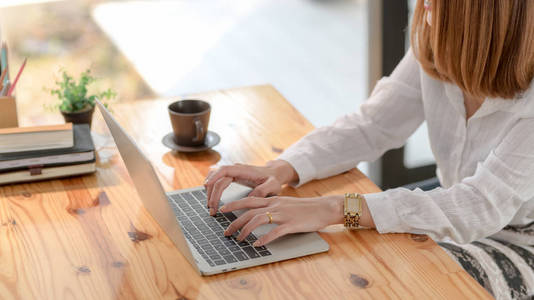 Cropped shot of a woman typing on laptop on wooden desk while si