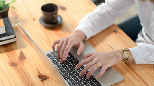 一个女人在木制桌子上的笔记本电脑上打字