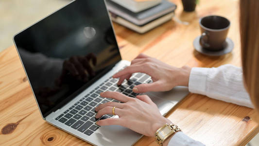 Cropped shot of a woman typing on laptop on wooden desk 